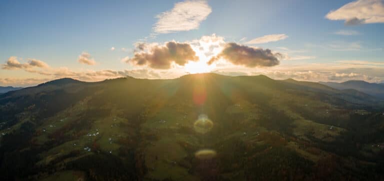 Aerial view of small shepherd houses on wide meadow between autumn forest in Ukrainian Carpathian mountains at sunset